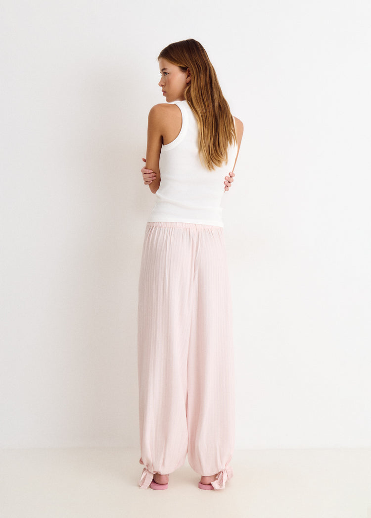 Pantalón largo bombacho de color rosa con pinzas y puños anudados, visto desde la espalda