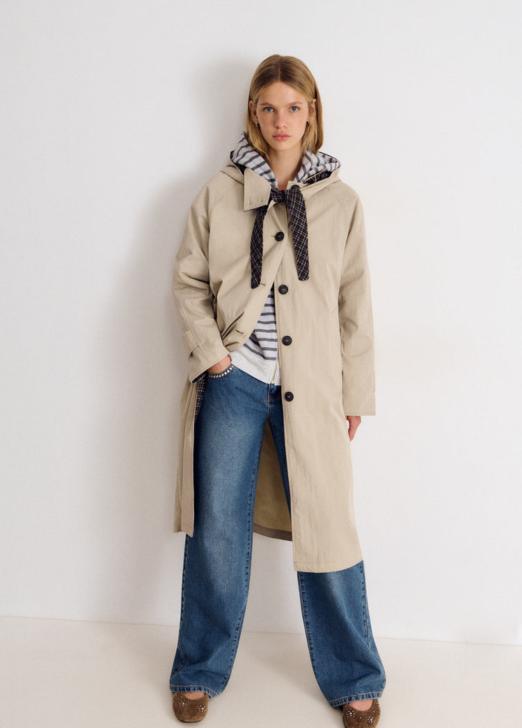 Chaqueta larga tipo gabardina en beige con capucha y botones oscuros vista de frente