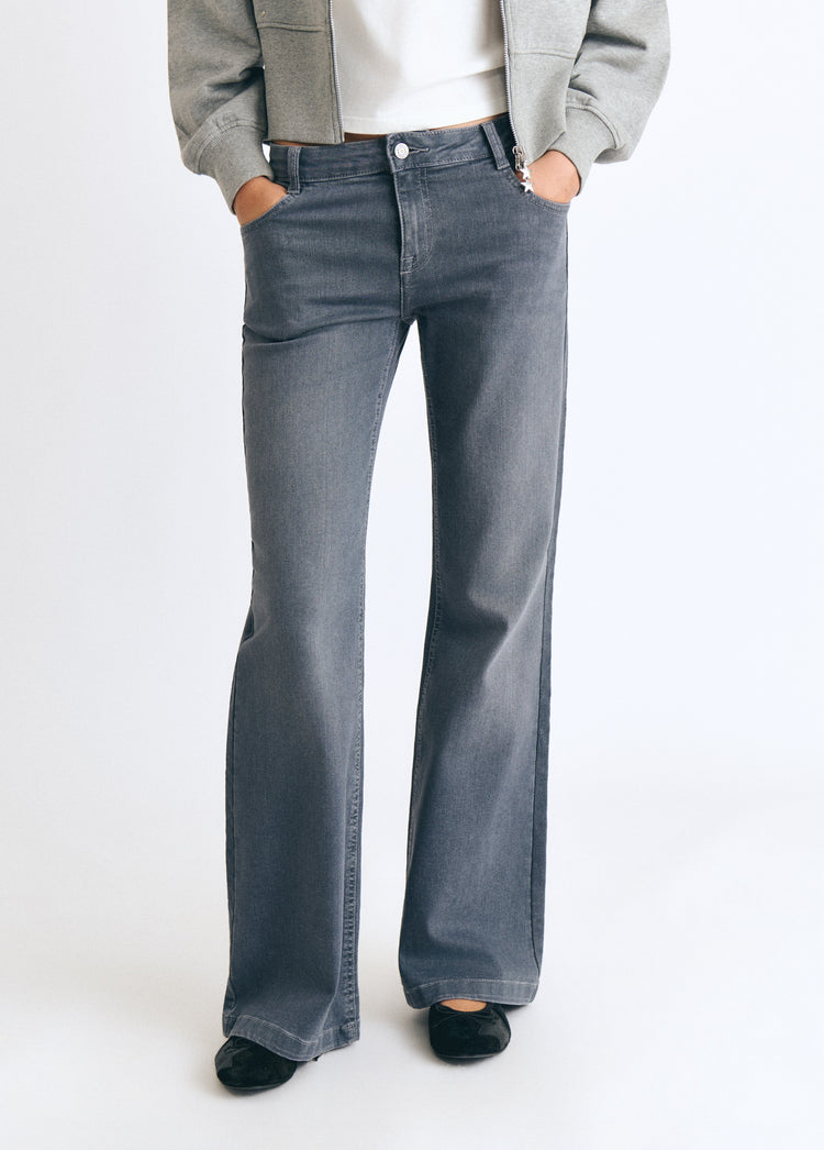Jeans flare de gris vistos de frente sobre modelo con chaqueta