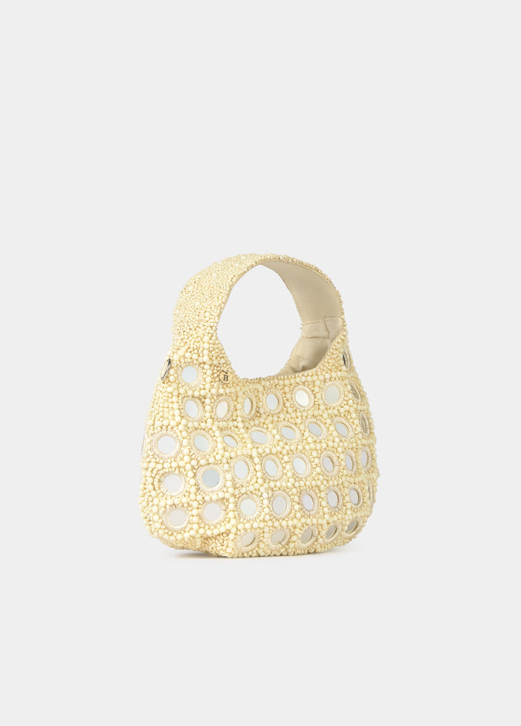 Bolso pequeño de color crudo con apliques de cuentas y espejos, visto de frente sobre fondo liso