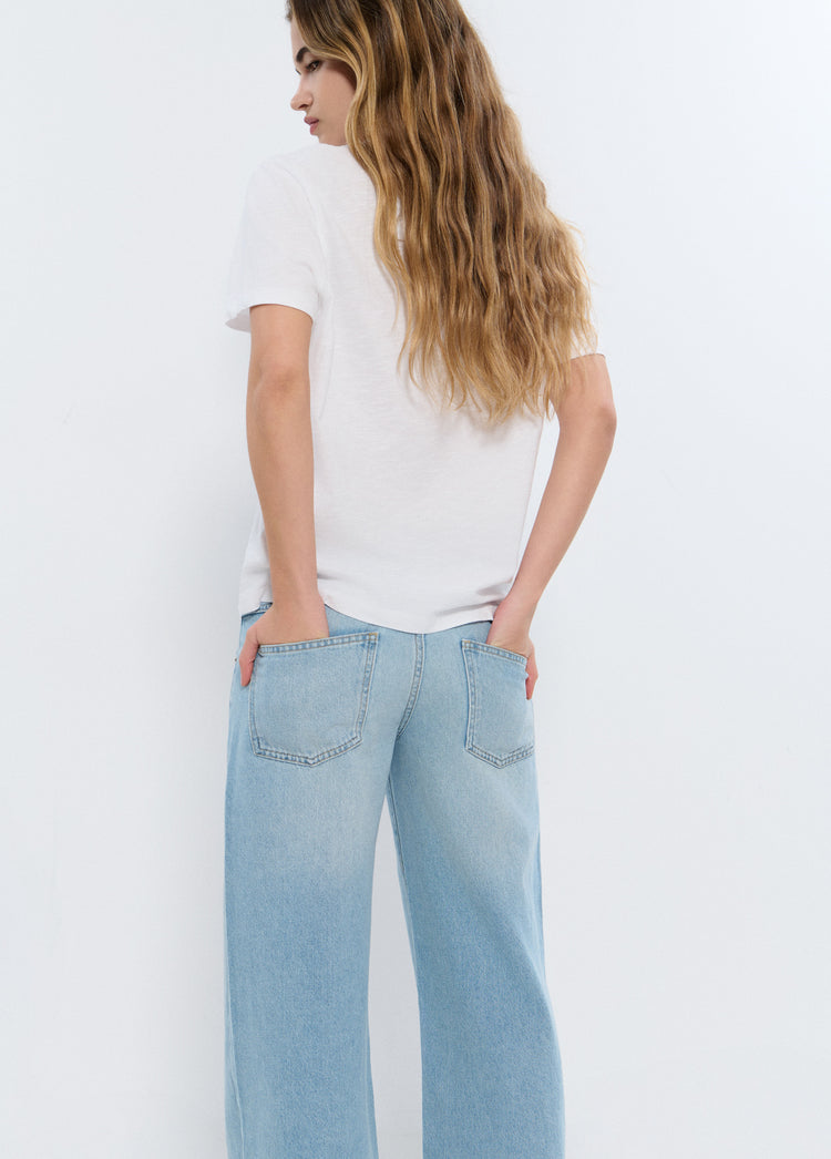 Camiseta básica de algodón blanco vista por detrás con las manos en los bolsillos de los vaqueros