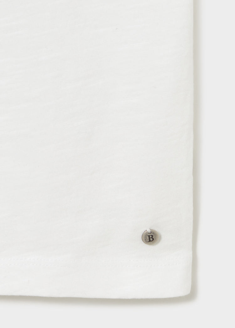 Detalle del puño de la camiseta de algodón blanco con botón metálico grabado