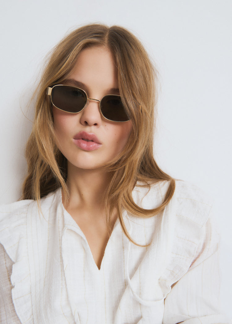 Gafas de sol de montura ovalada en color dorado lucidas sobre el rostro