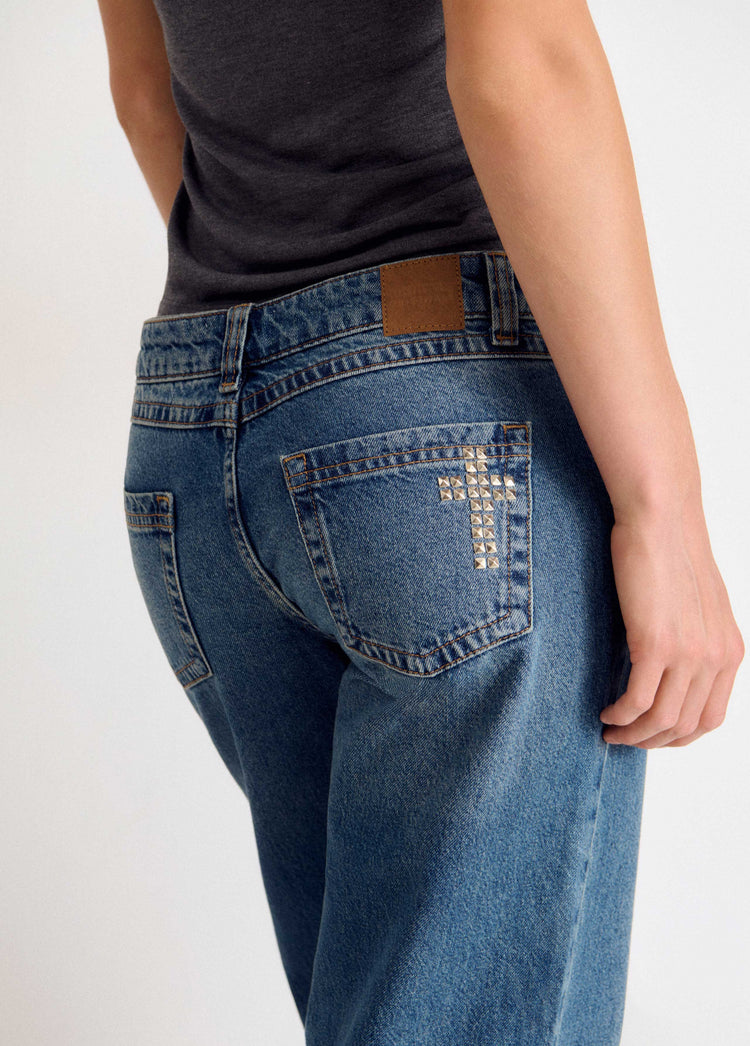 Jeans de color azul medio vistos por detrás con tachas en cruz sobre el bolsillo trasero