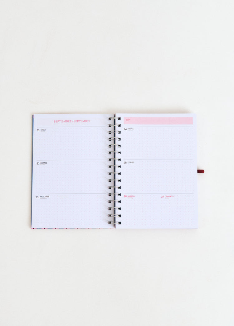 Agenda escolar planner de espiral abierta mostrando las páginas de septiembre en color rosa sobre fondo blanco