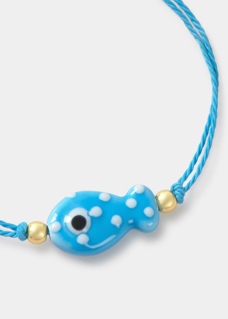 Pulsera azul de hilo con colgante de pez y detalles dorados sobre fondo liso