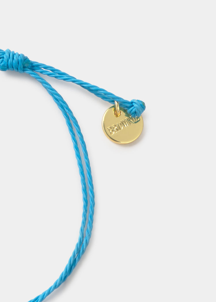 Pulsera de hilo azul con colgante dorado grabado en primer plano sobre fondo liso