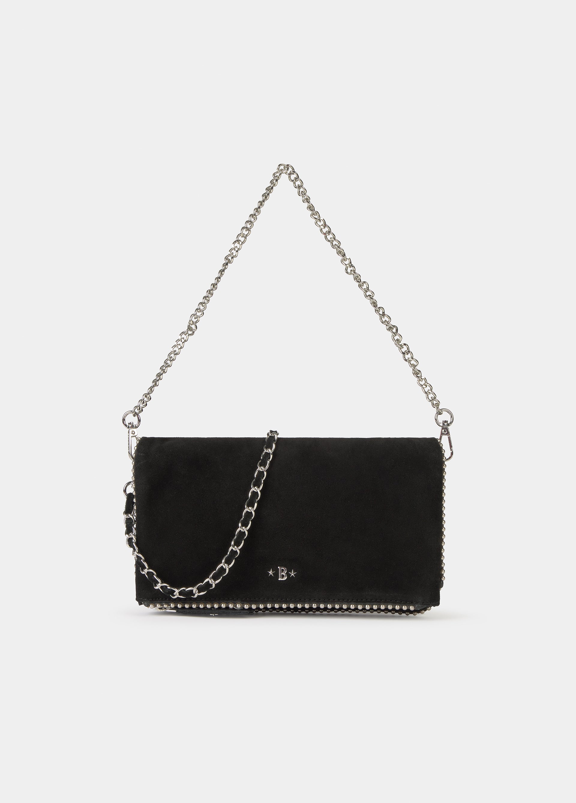 Bolso negro de solapa con bolitas de serraje colgado de la mano sobre fondo blanco