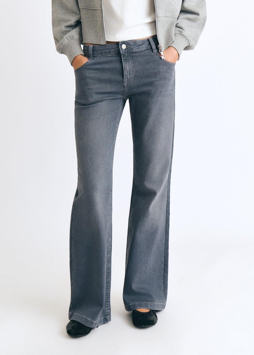 Jeans flare de gris vistos de frente sobre modelo con chaqueta