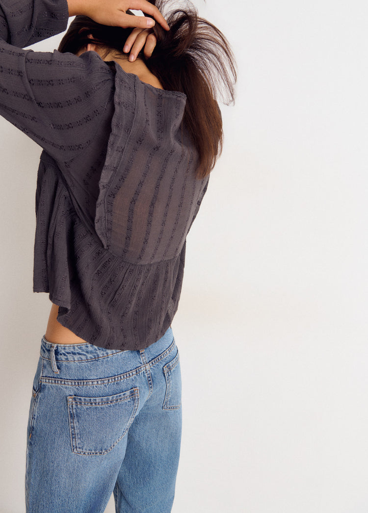 Blusa de manga larga en gris vista por detrás con el dobladillo asomando sobre los vaqueros
