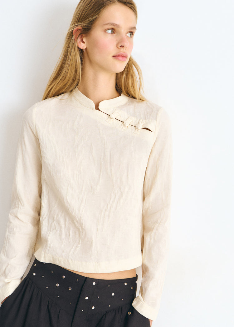 Blusa de manga larga en color crudo con cuello alto y detalle de botones en el pecho