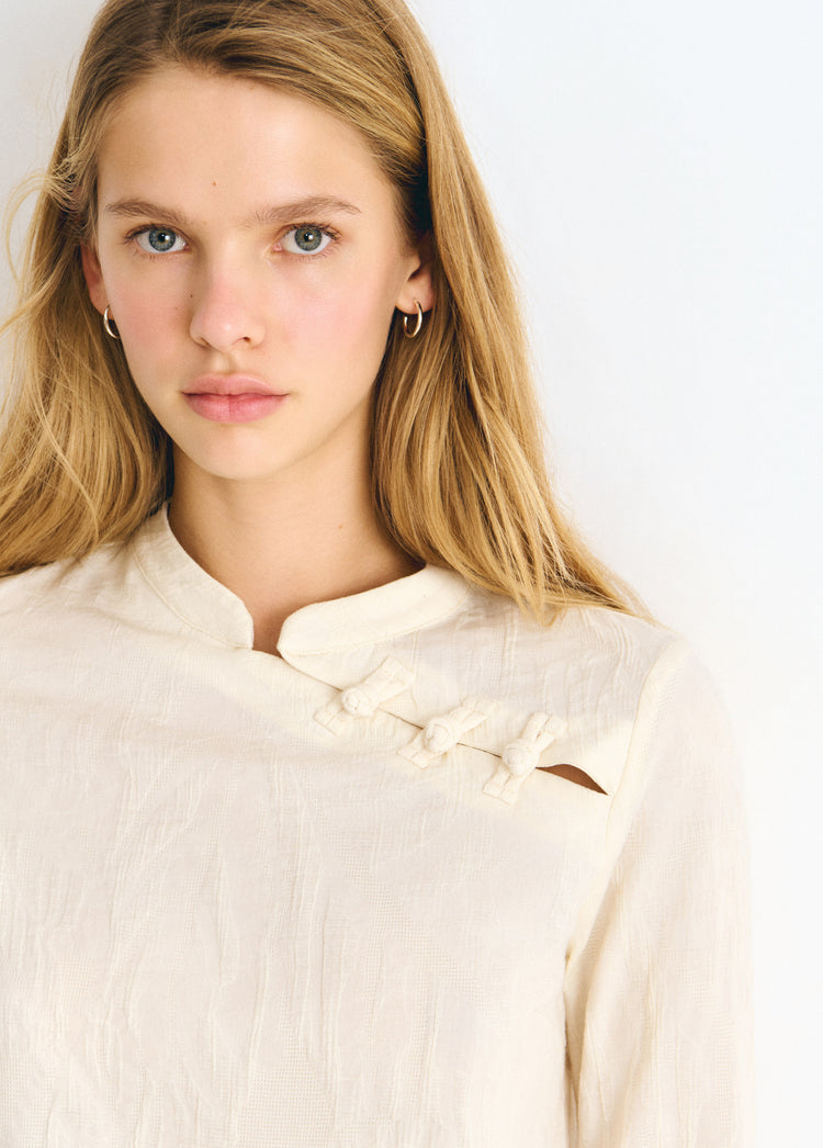 Blusa de tejido jacquard en tono crudo con cierre de botones decorativos en el escote